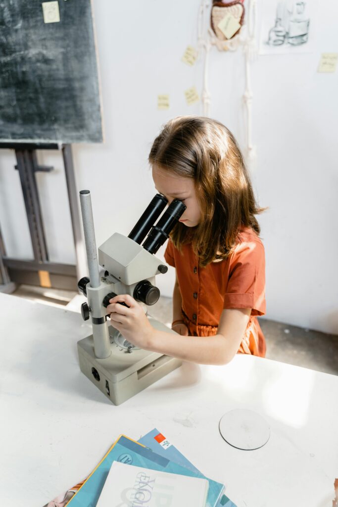 pexels-photo-8471910-8471910 A curious young girl examines a specimen with a microscope in a classroom setting.